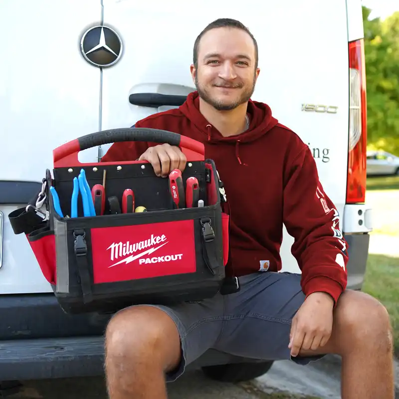 Plumber sitting on a bumper holding tools